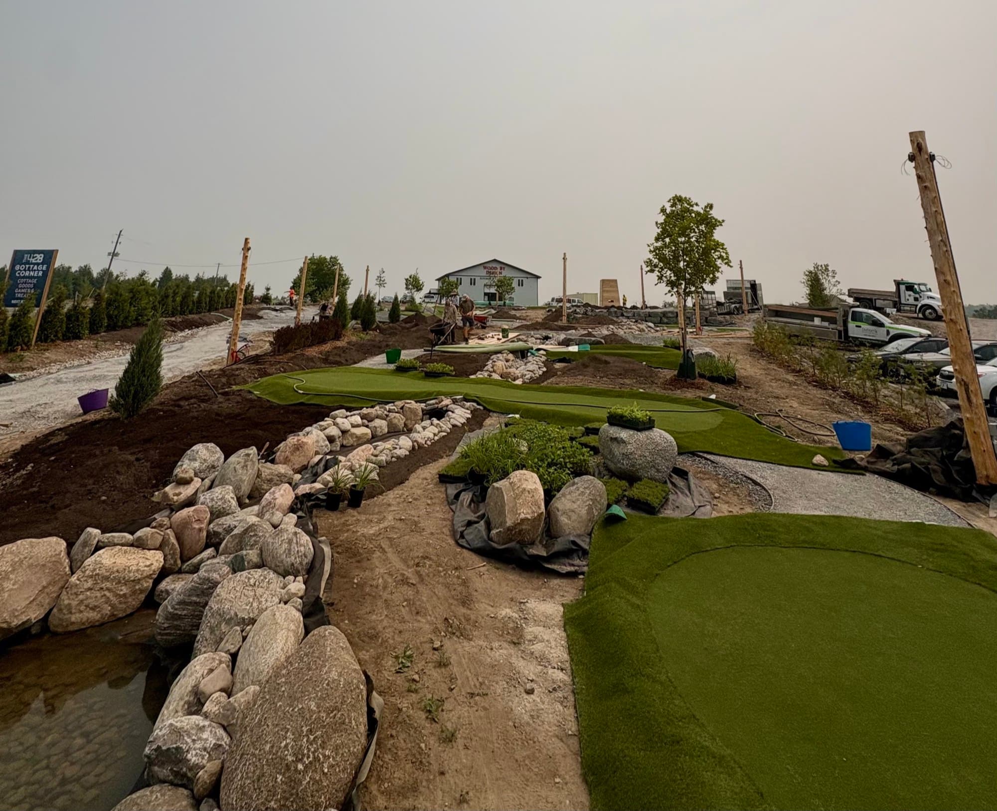 The Little Mini Golf Co course under construction, with turf greens, boulders, and a pond